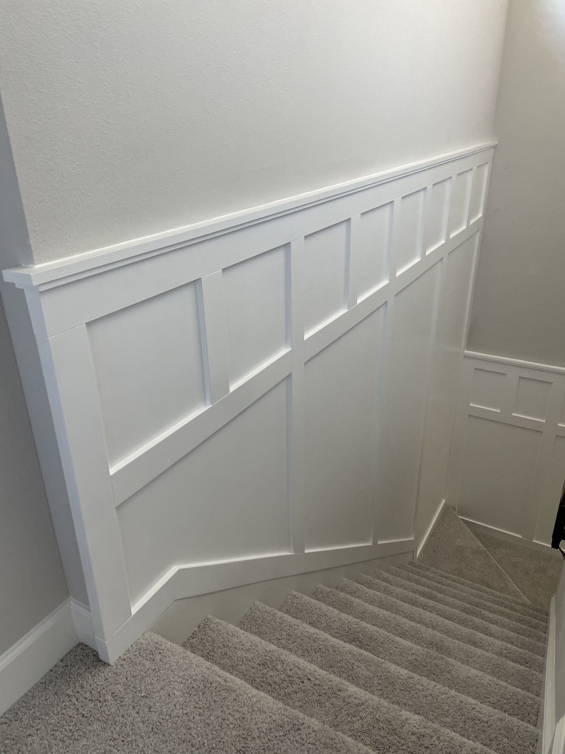 White paneled wall with stairs descending; the wall has molding at the top, the stairs are carpeted.
