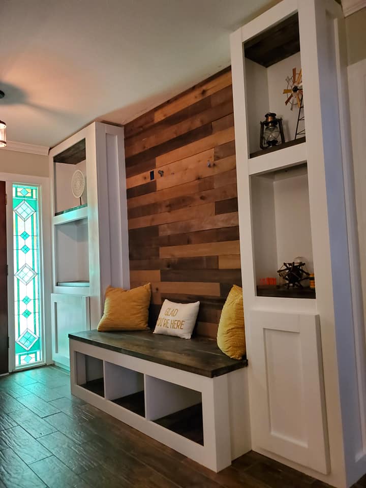 Entryway with wood plank accent wall, built-in bench, storage cubbies, and white shelving units.