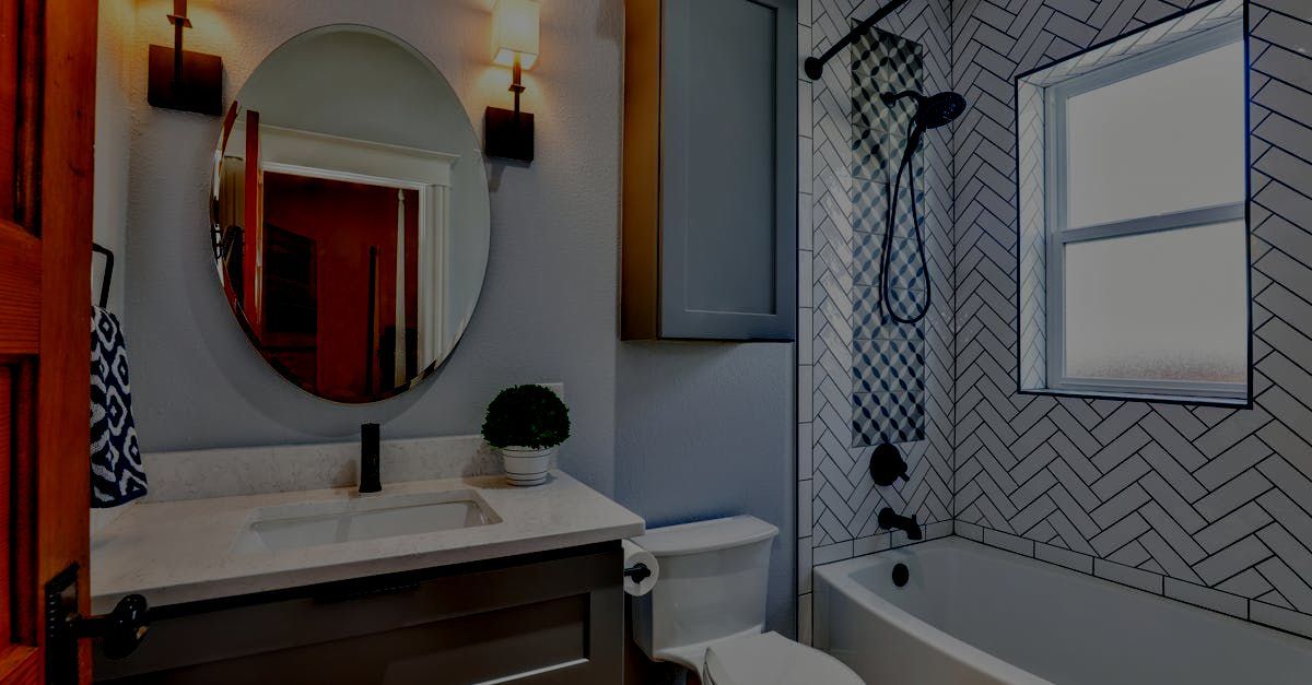Bathroom with a round mirror, gray vanity, white toilet, and a herringbone-tiled shower area.