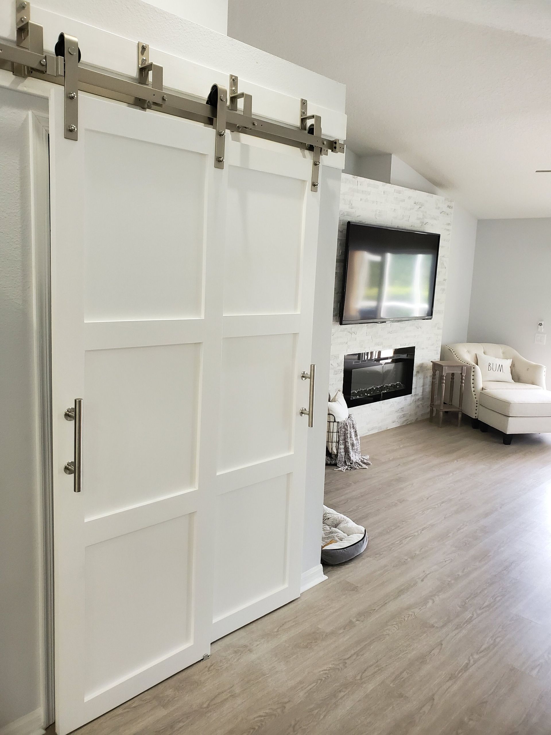 White sliding barn door, stainless steel hardware, opening into living room with fireplace and couch.