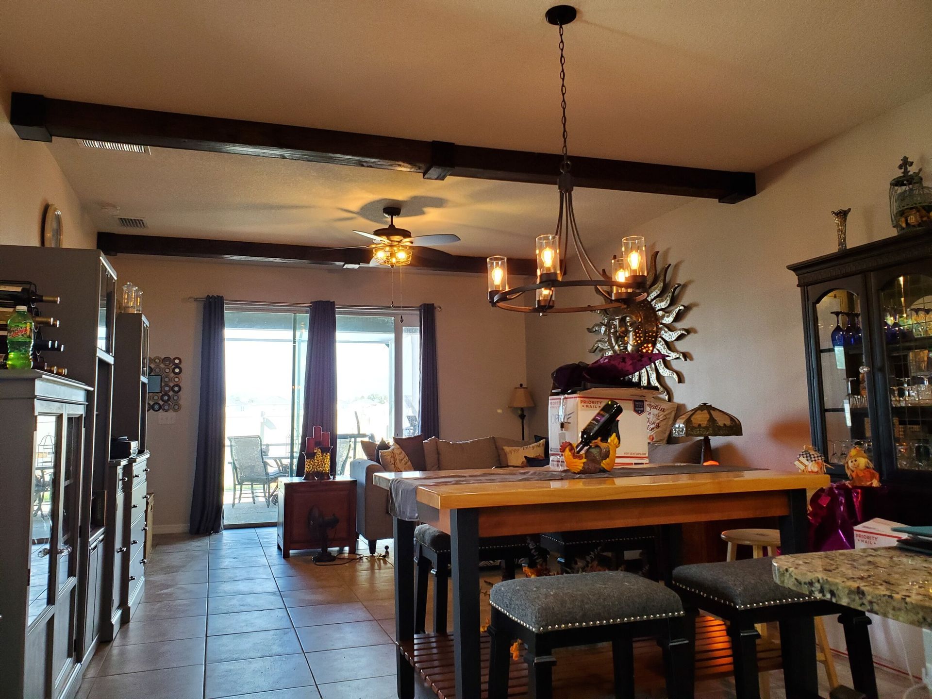 A living room with dark wood beams, a chandelier over a dining table, and a view to a patio.
