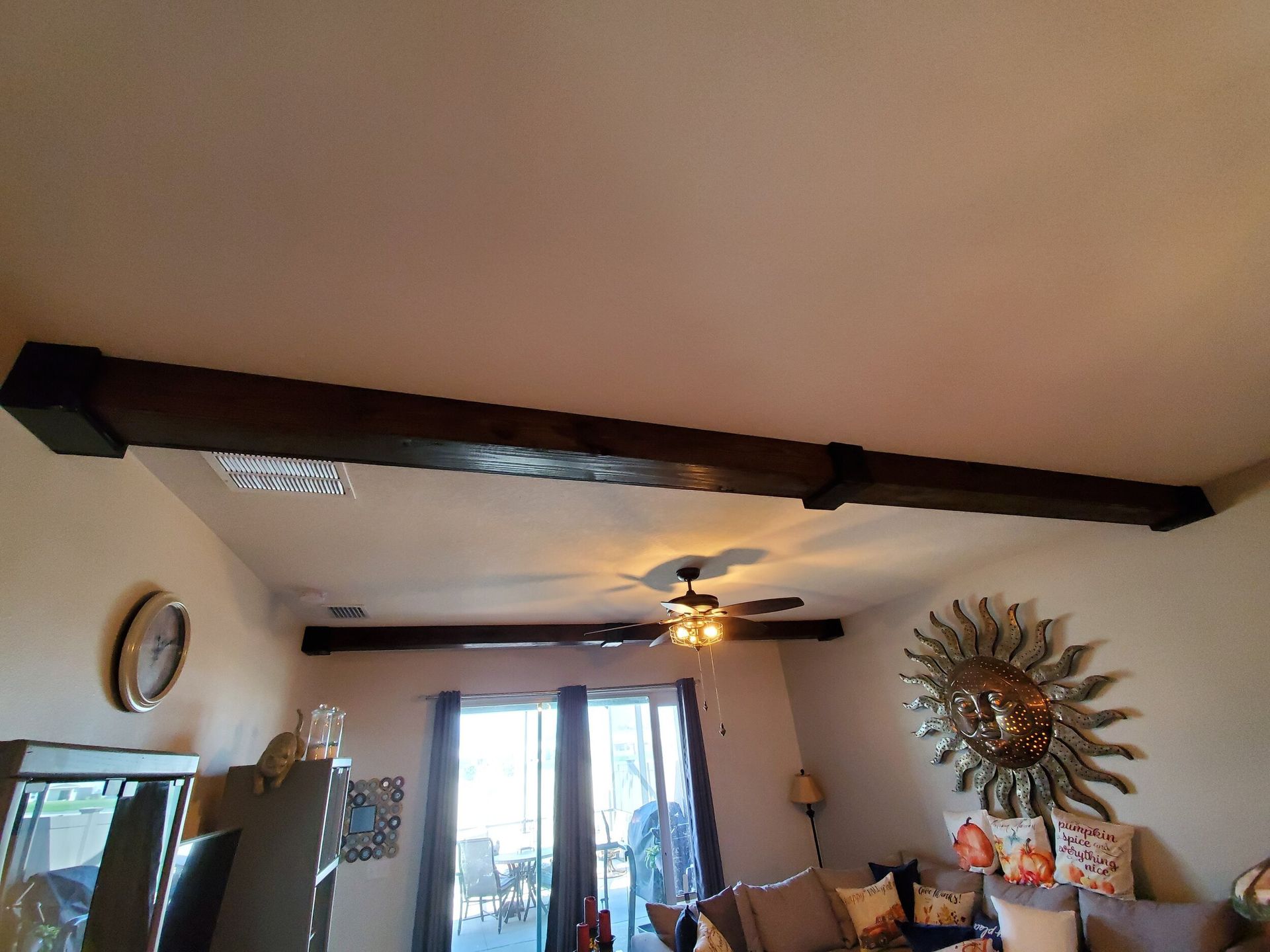 Wooden beams on a ceiling with a decorative sunburst mirror and a clock.