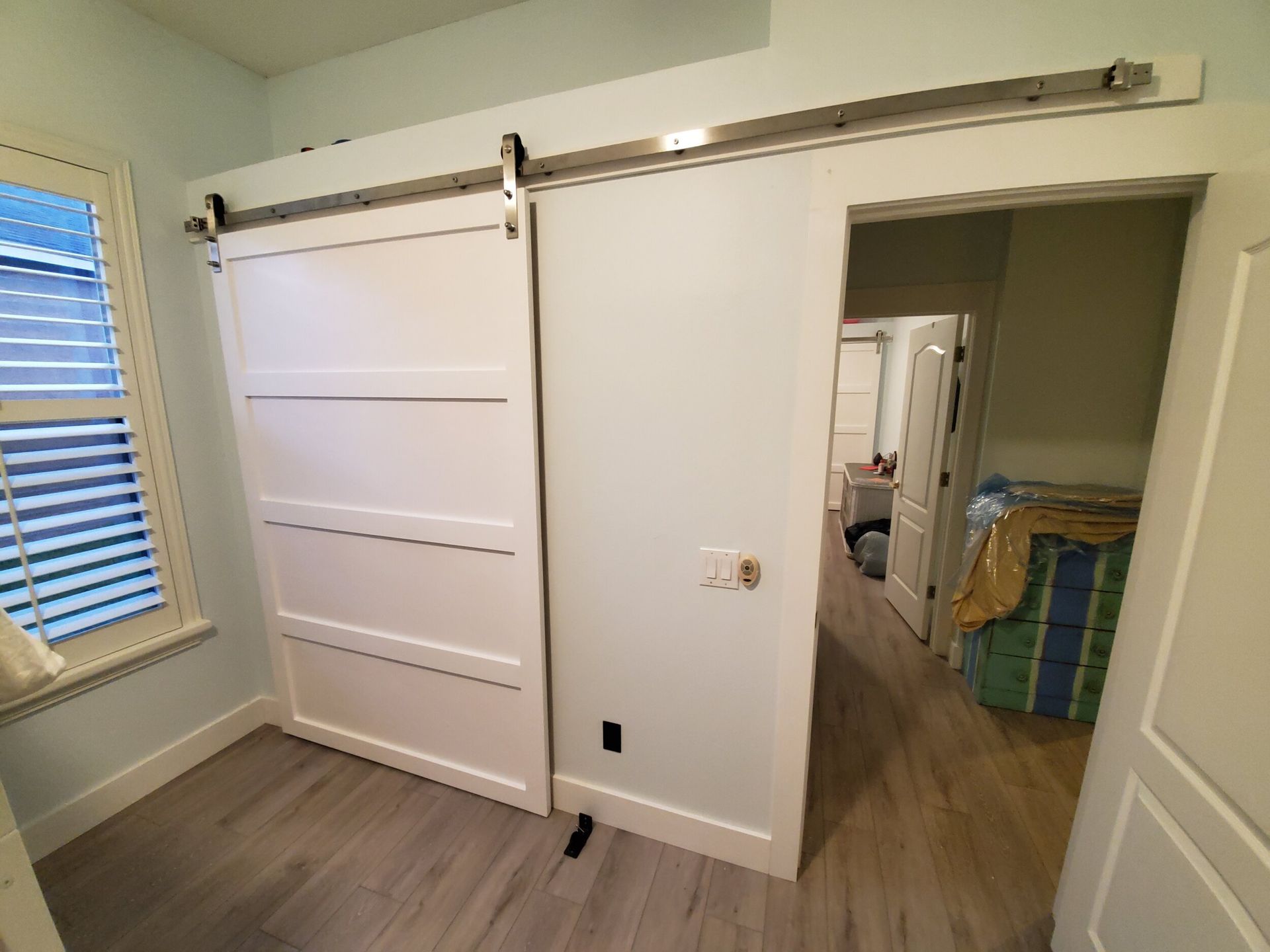White sliding barn door partially closed, leading to hallway. Light blue walls, wood floor.