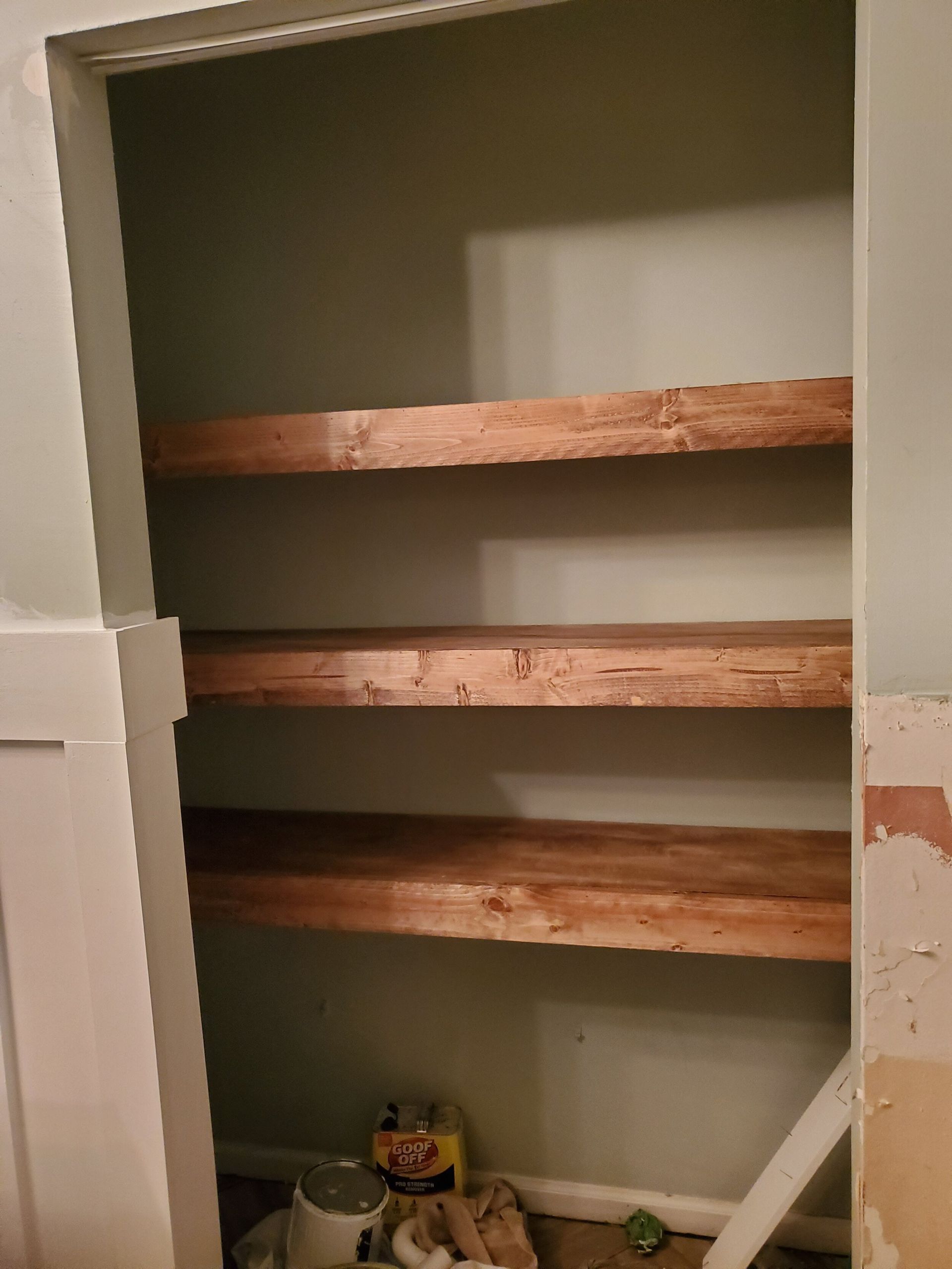 A small closet with three wooden shelves against a light green wall.