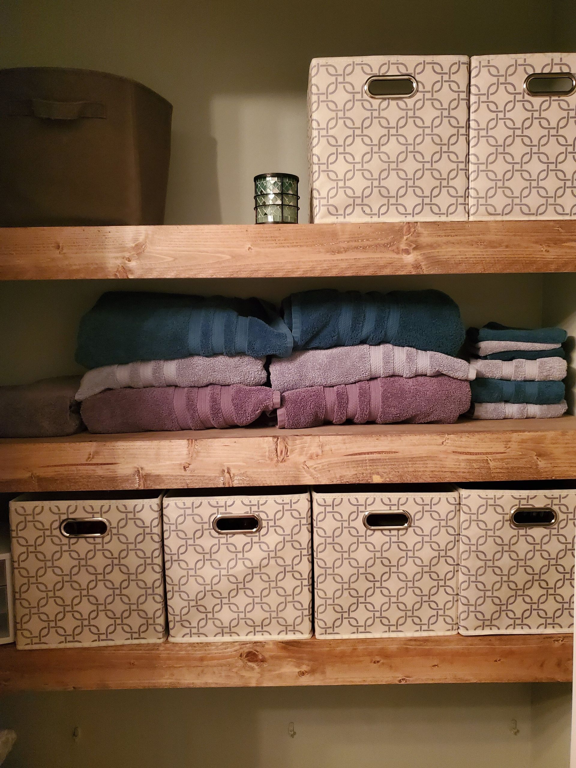 Shelves in a closet holding folded towels, patterned boxes, and a brown basket.