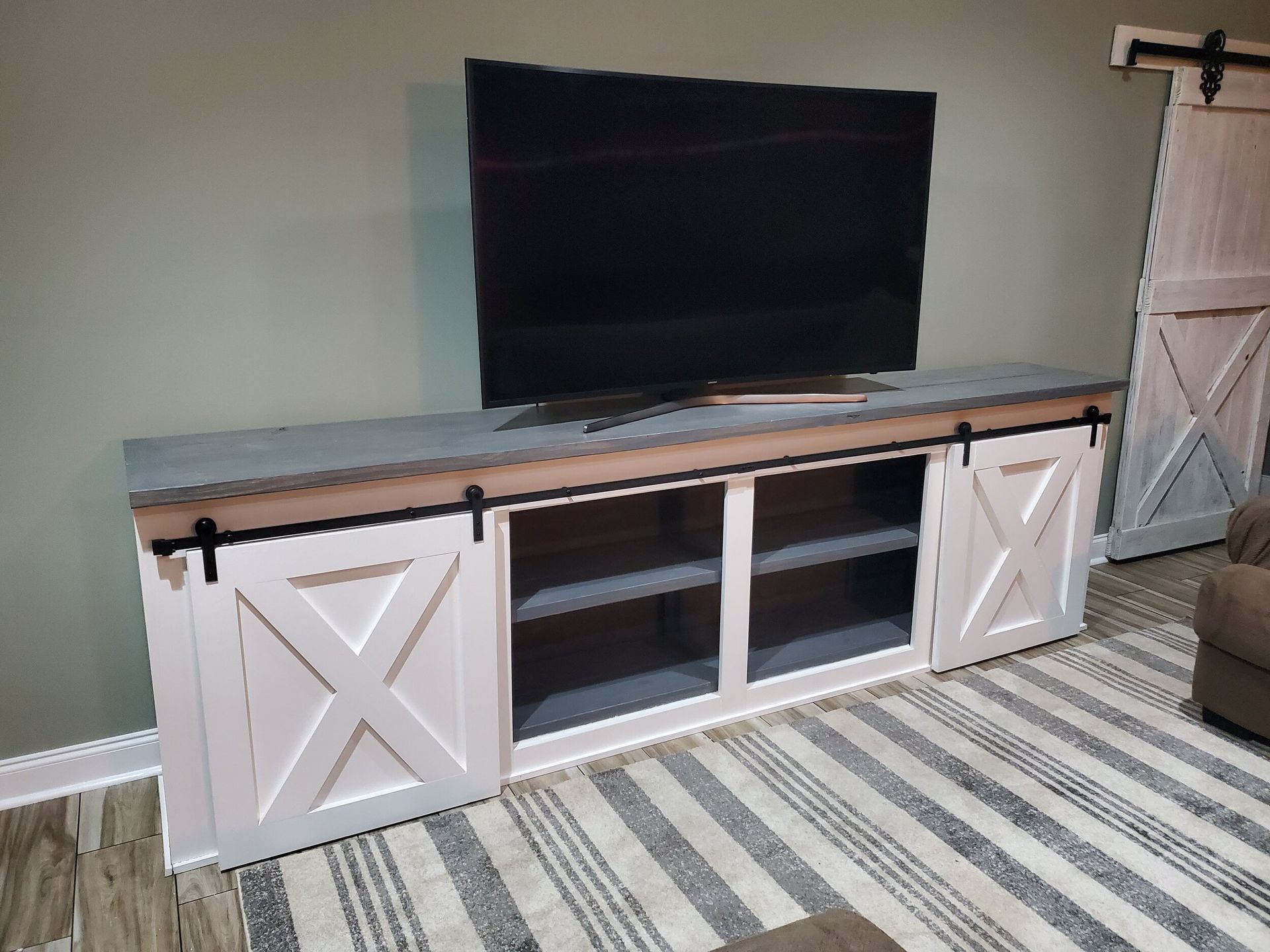 TV on a white cabinet with sliding barn doors and a gray countertop, on a striped rug.
