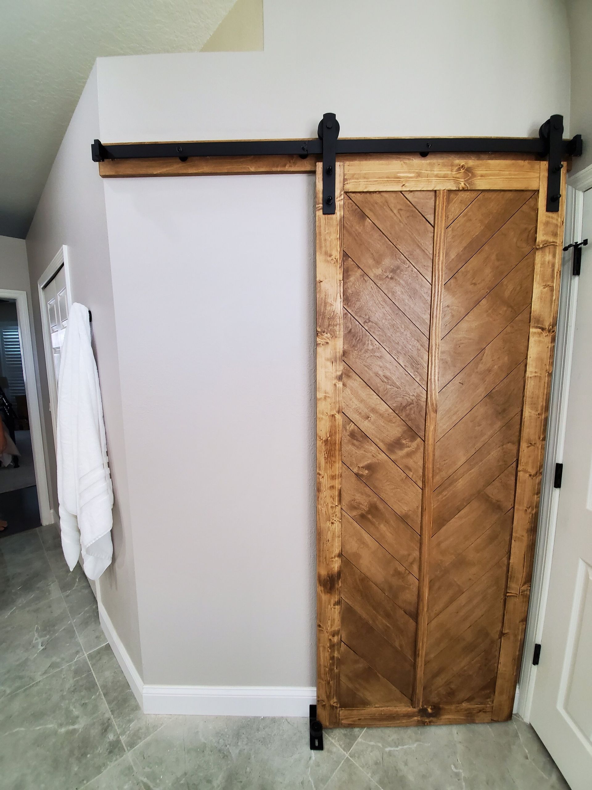 Barn door with chevron wood pattern. Brown, black hardware; gray walls and floor.