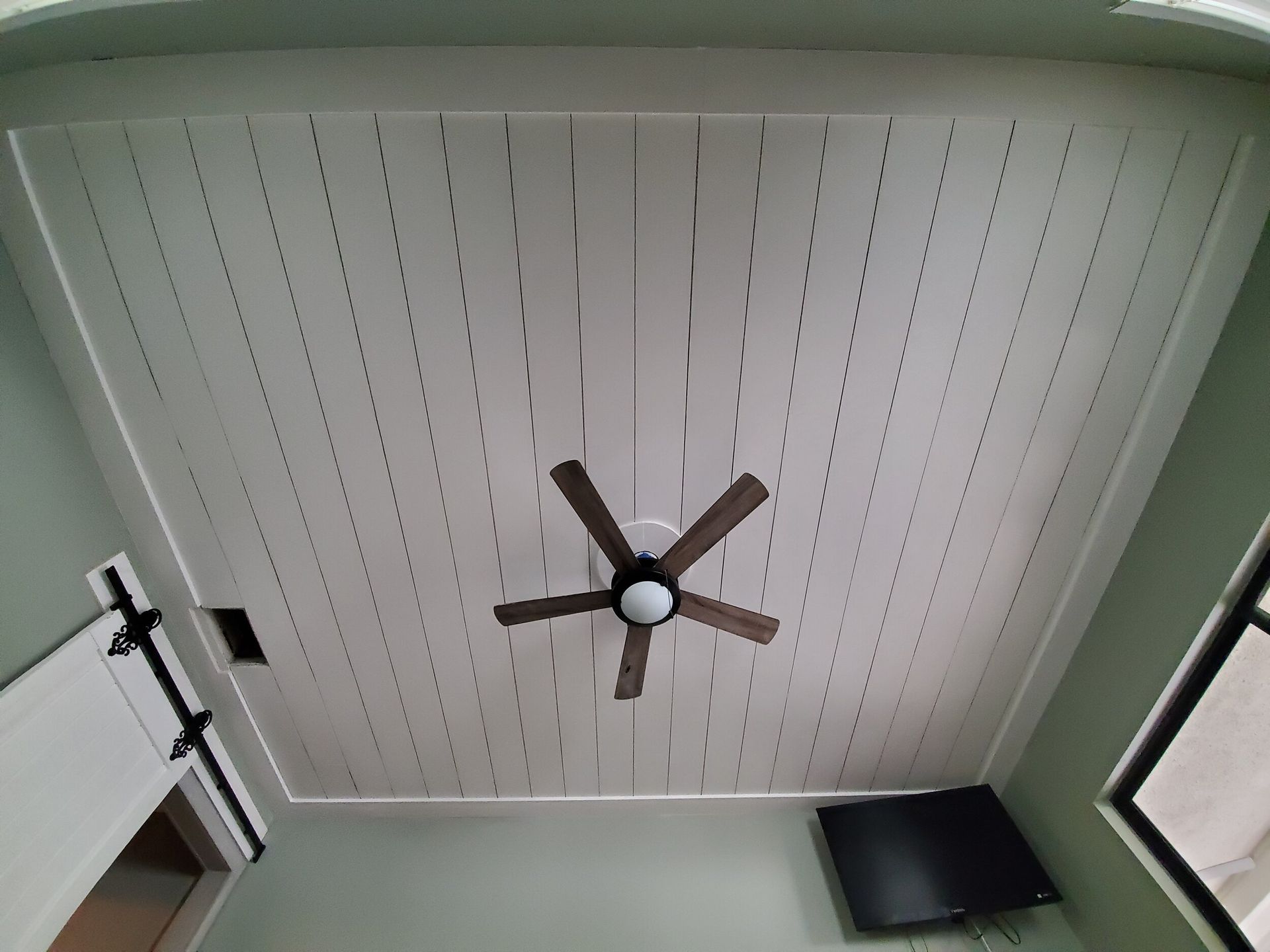 White paneled ceiling with a ceiling fan, and a wall-mounted TV in a room.