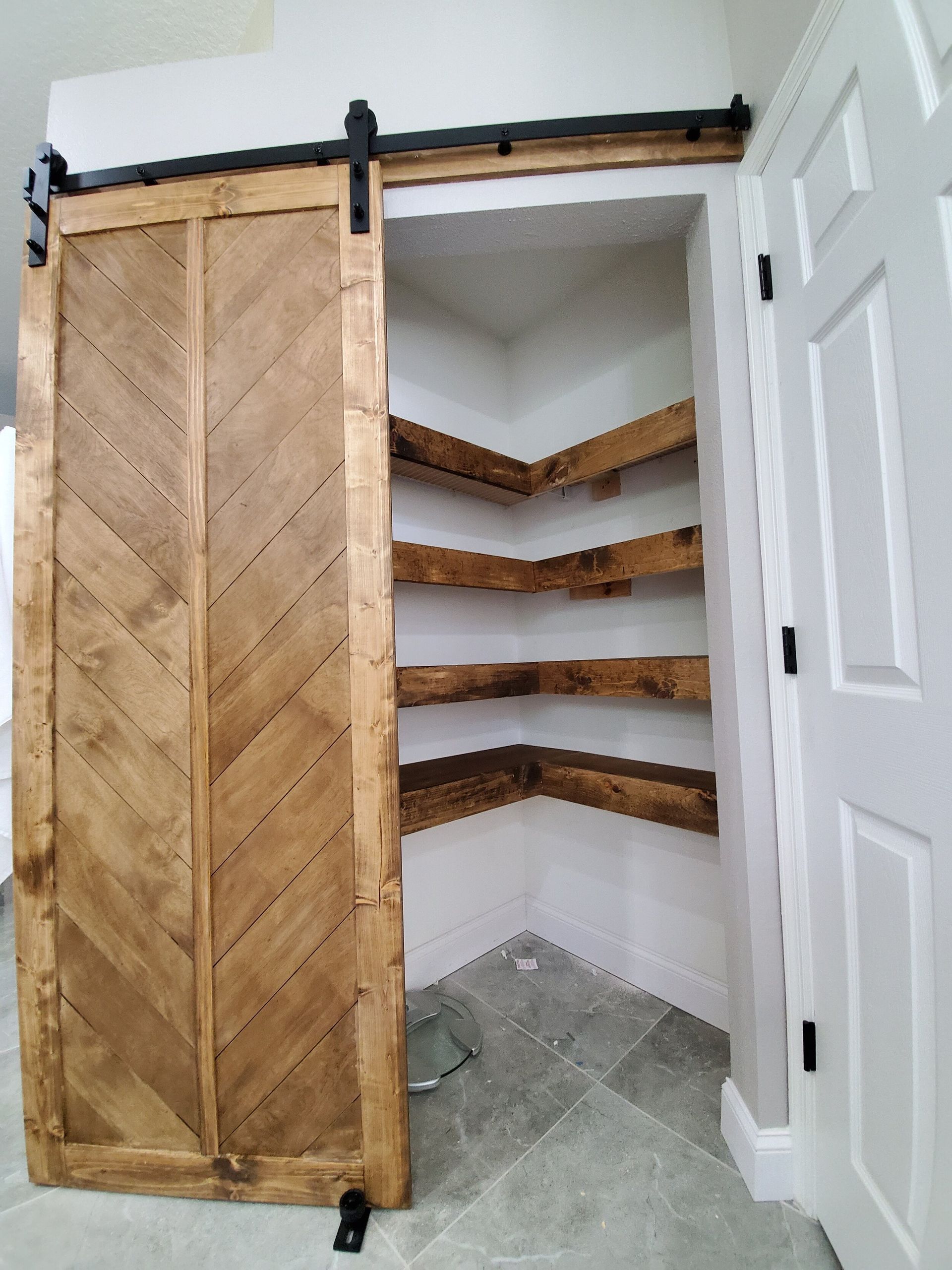 A rustic, wooden sliding barn door opens to a pantry with corner shelves.