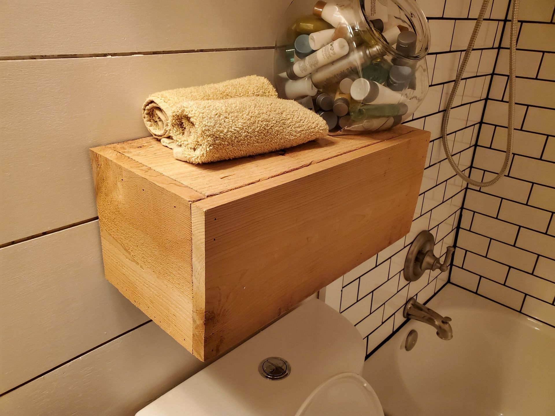 Wooden shelf with towels and toiletries above a toilet in a bathroom.