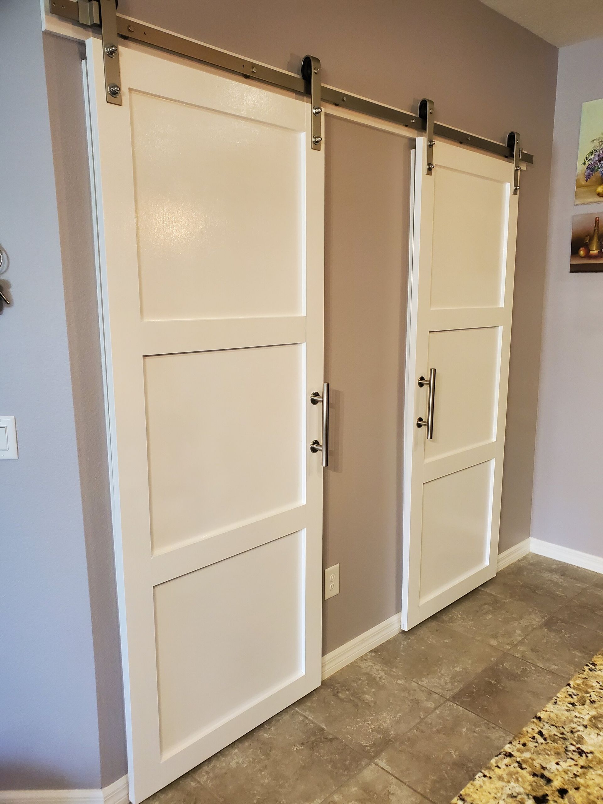 White barn doors on a gray wall, with dark hardware. The floor is tiled.