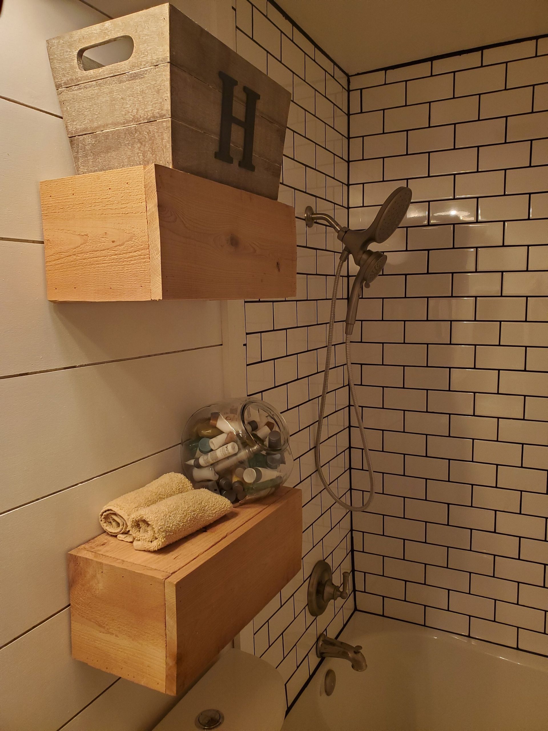 Bathroom with wood shelves holding towels, a jar of items, and a box with the letter 