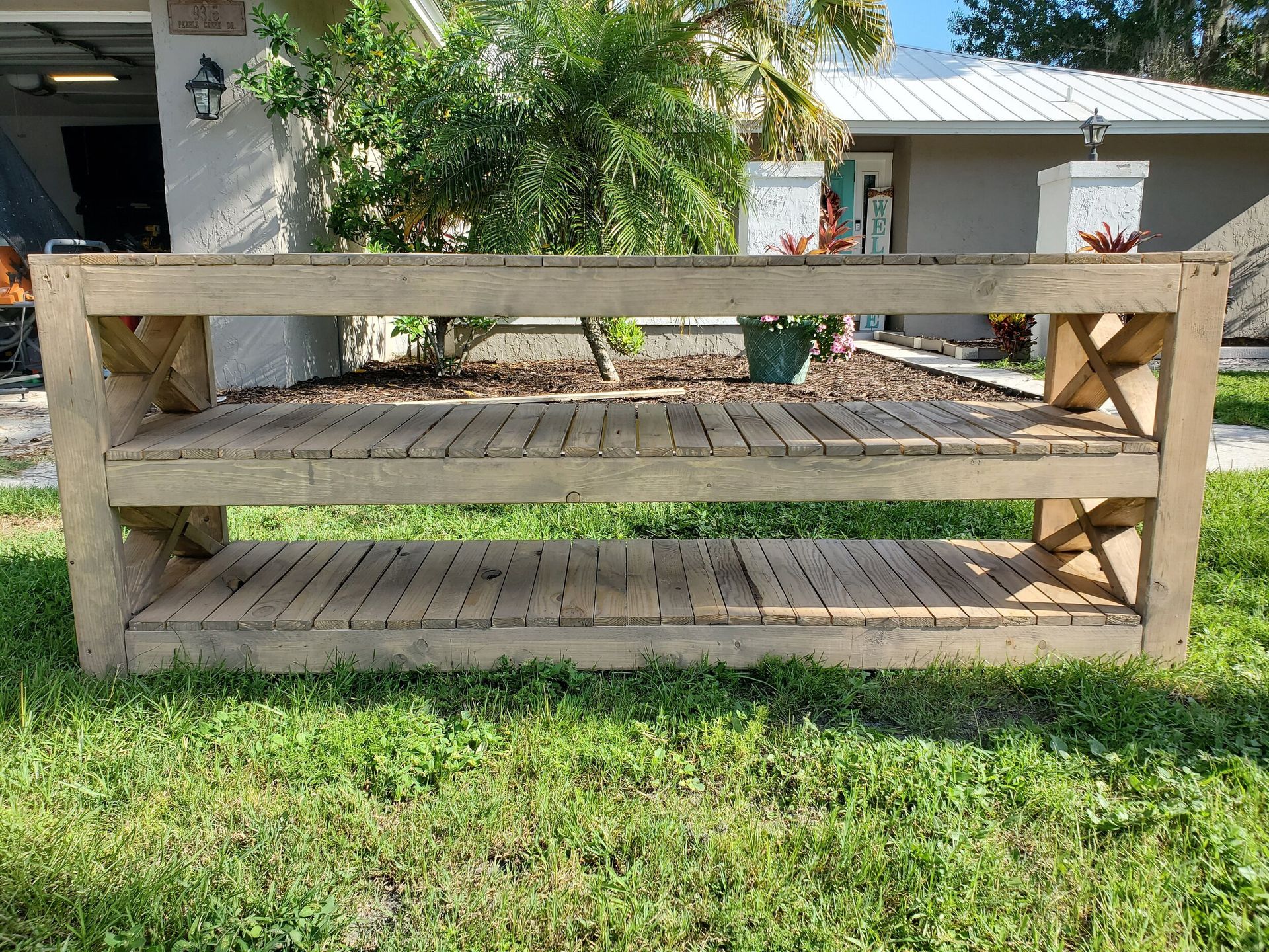Rustic wooden console table with two shelves, on grass in front of a house.