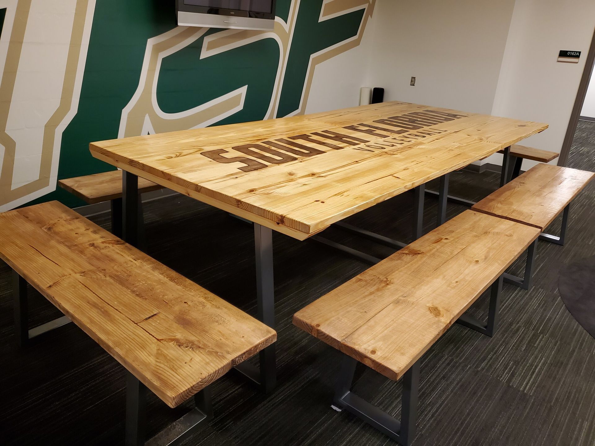 Wooden table and benches in room with USF logo on wall.