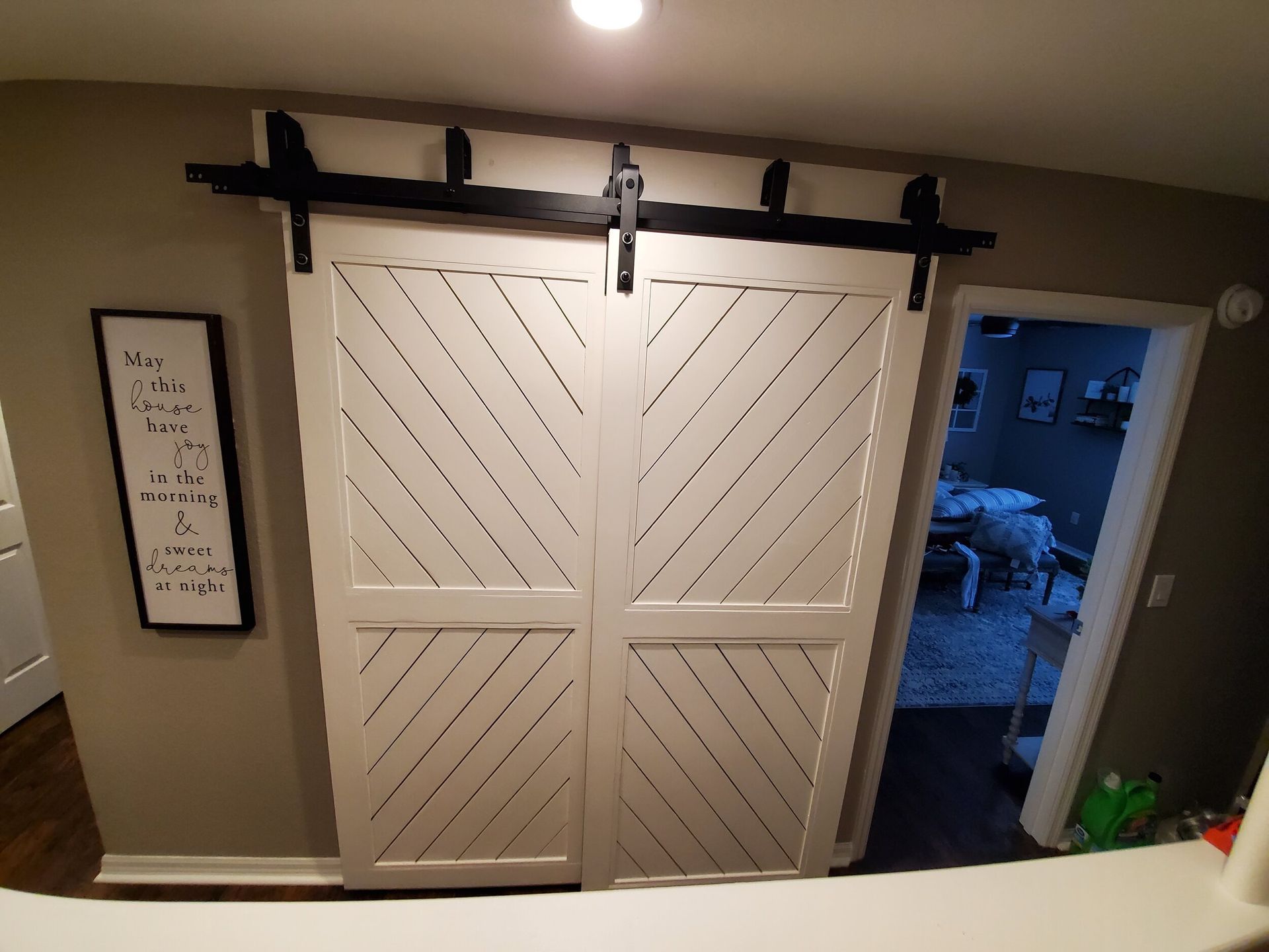 White, diagonal-slat barn doors with black hardware, leading to a room.