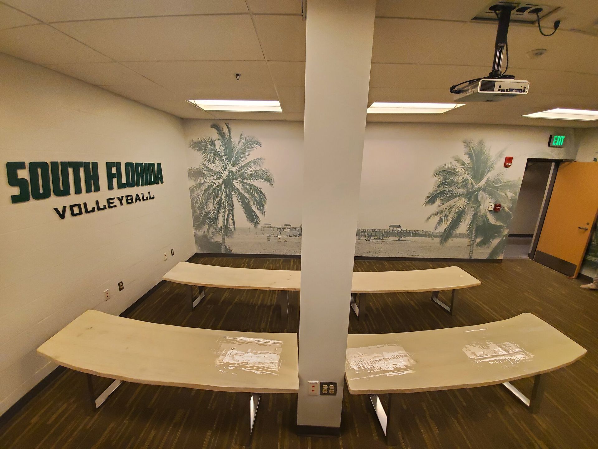 A classroom with curved tables, a pillar, palm tree murals, and 