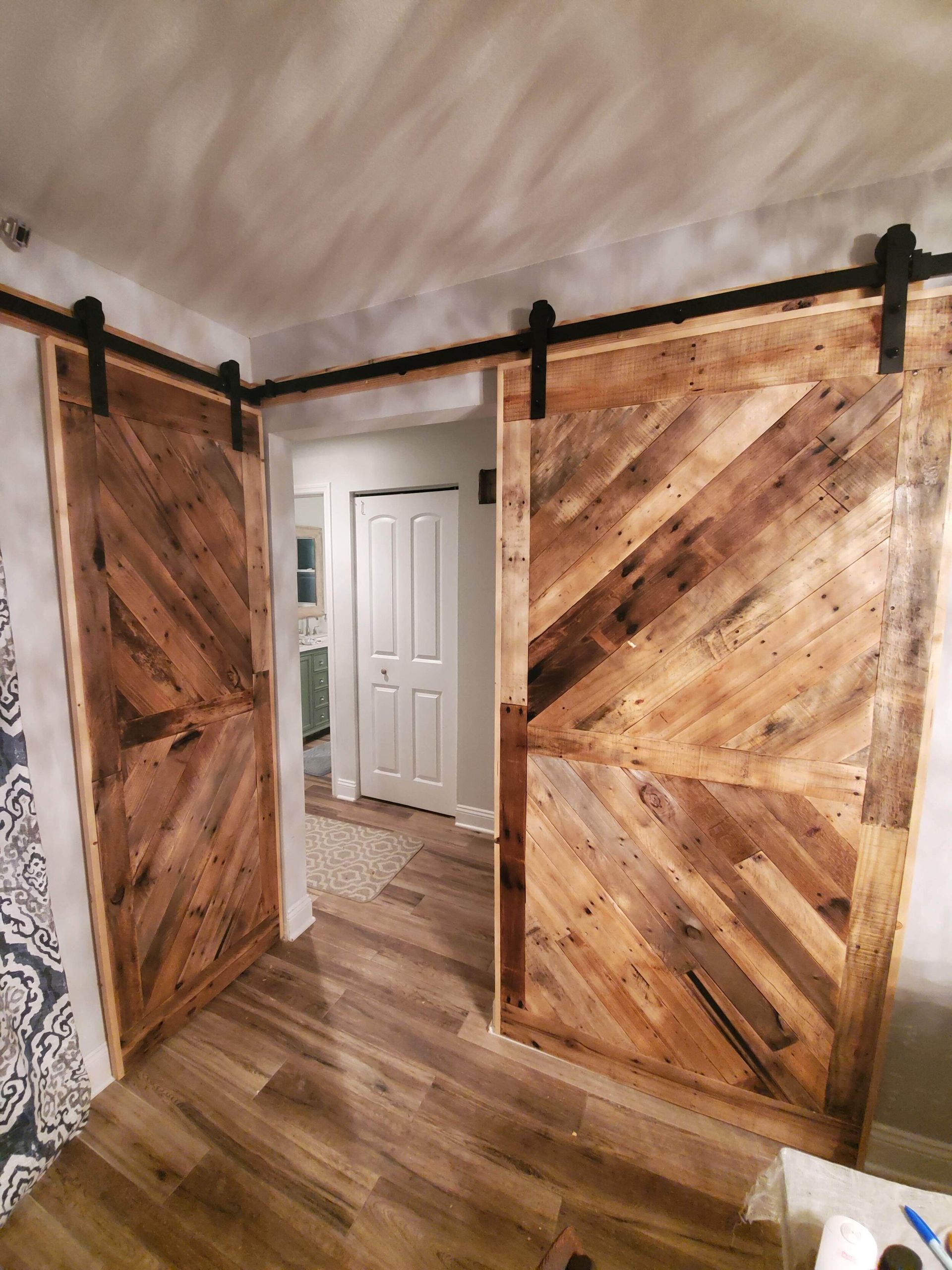 Barnwood-style sliding doors open to a hallway, brown wood pattern, black hardware, light wood floor.