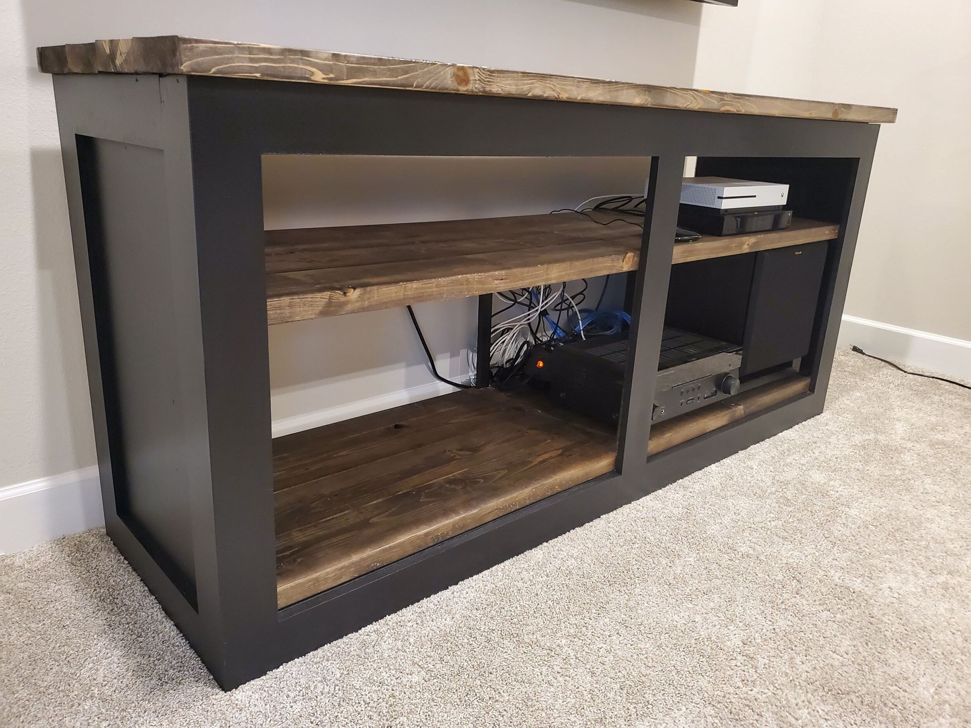 Dark gray and wood media console with open shelves on a beige carpet.