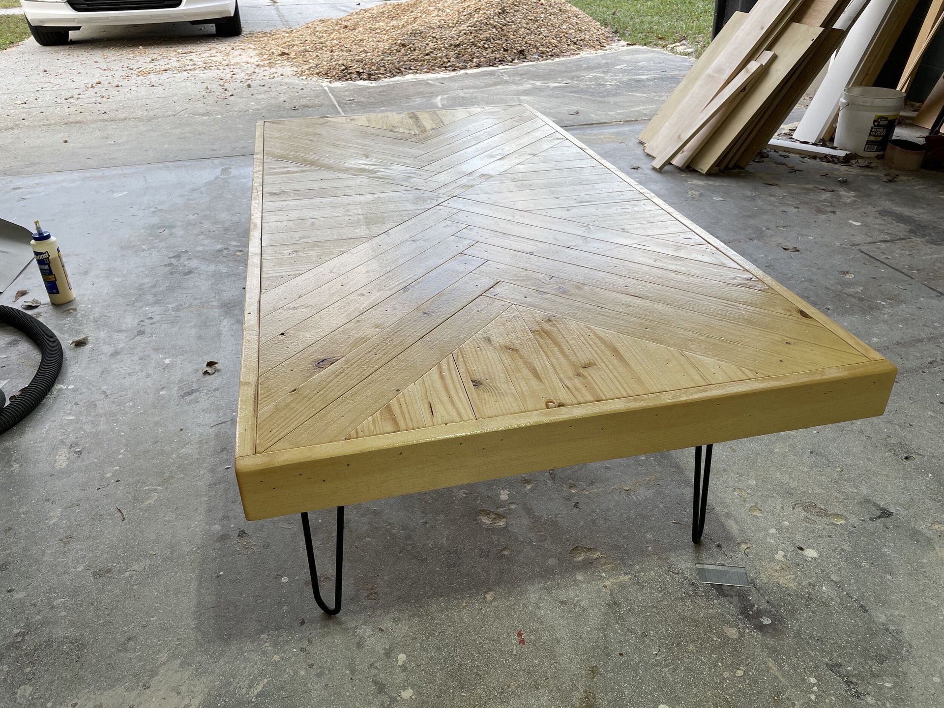 Wooden coffee table with black hairpin legs; outdoors on concrete. Top surface has small holes.