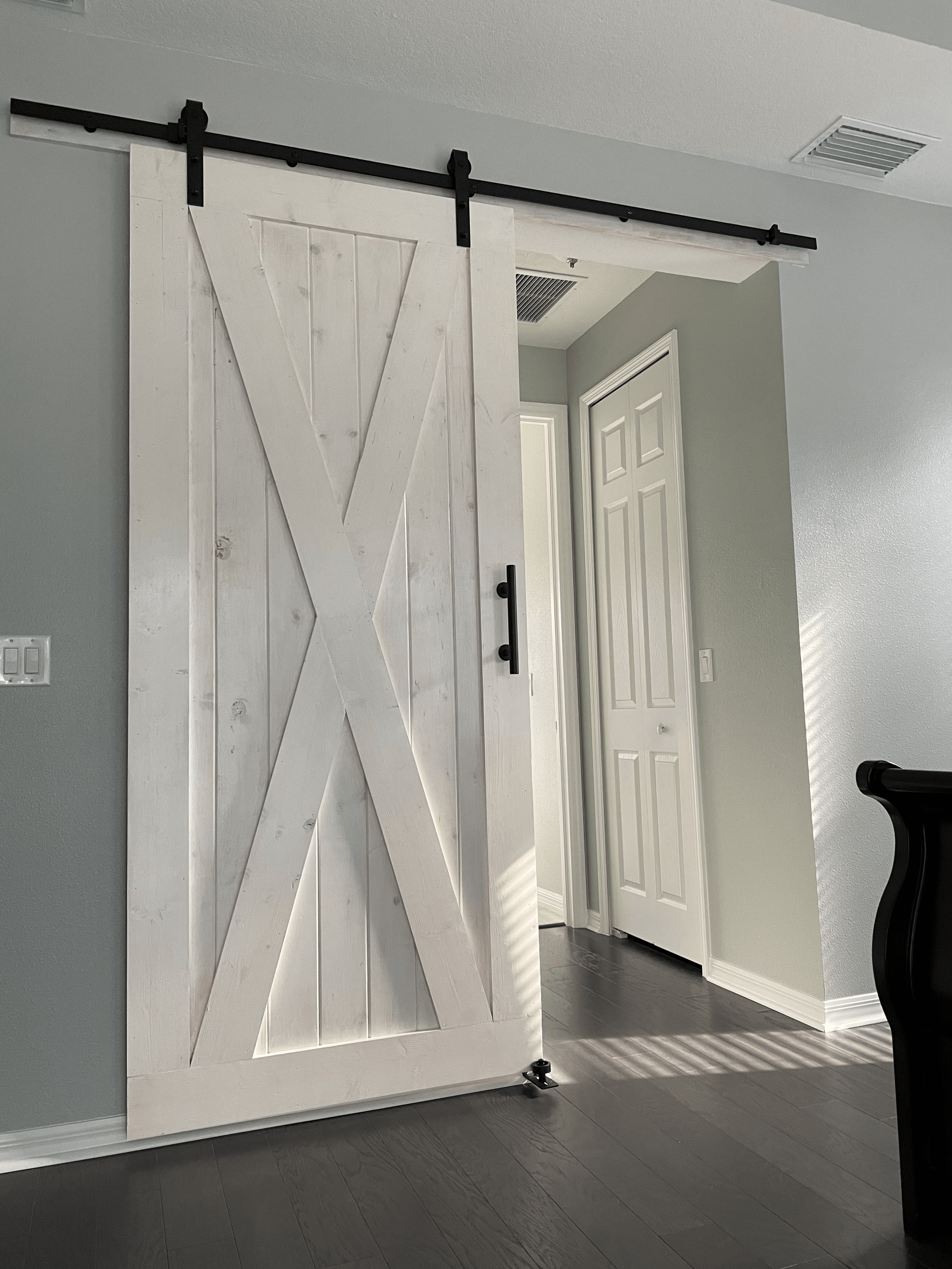 White barn door with black hardware, open to reveal hallway.