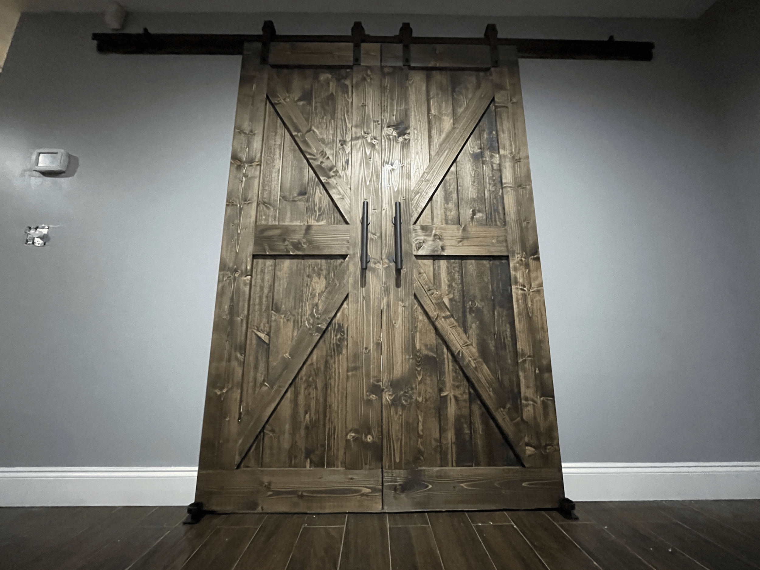 Rustic wooden barn doors on a gray wall, with black hardware.