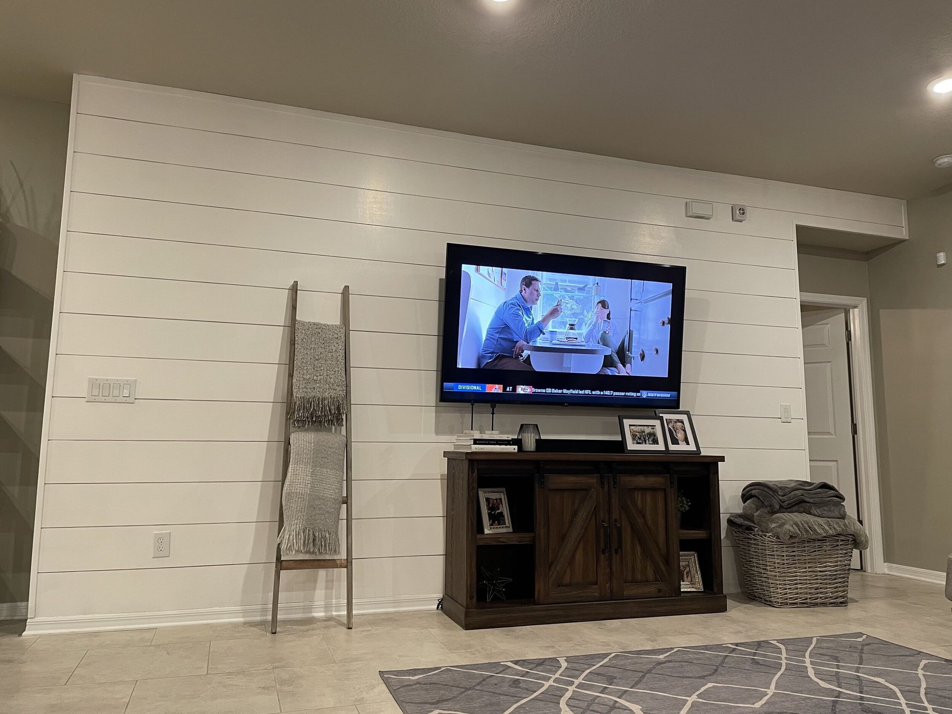 White shiplap wall with TV, wooden cabinet, and decorative ladder in living room.