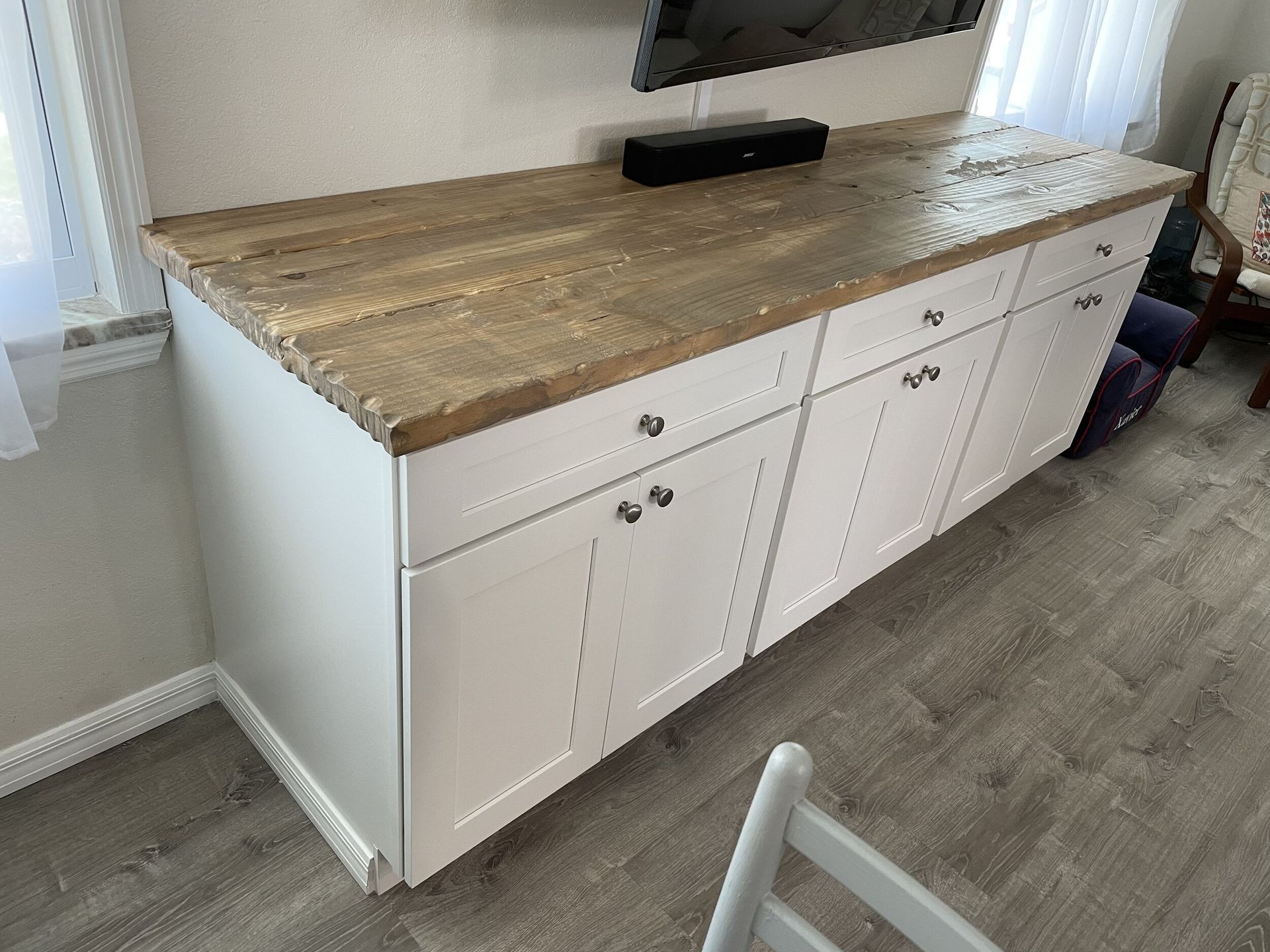 White cabinet with wood countertop under a TV. It has four doors and three drawers.