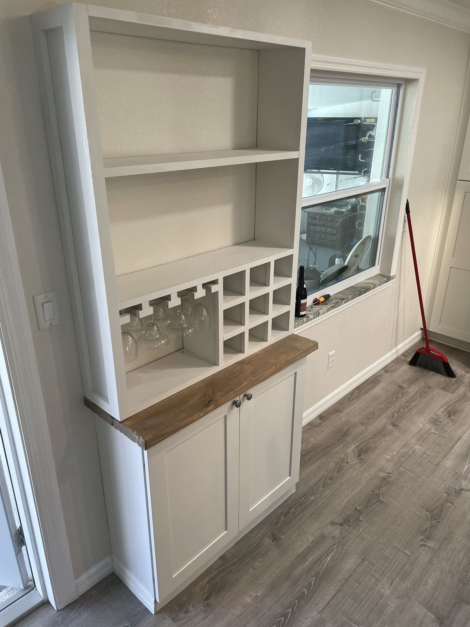 White cabinet with open shelves, wine rack, and lower cabinet, next to a window.