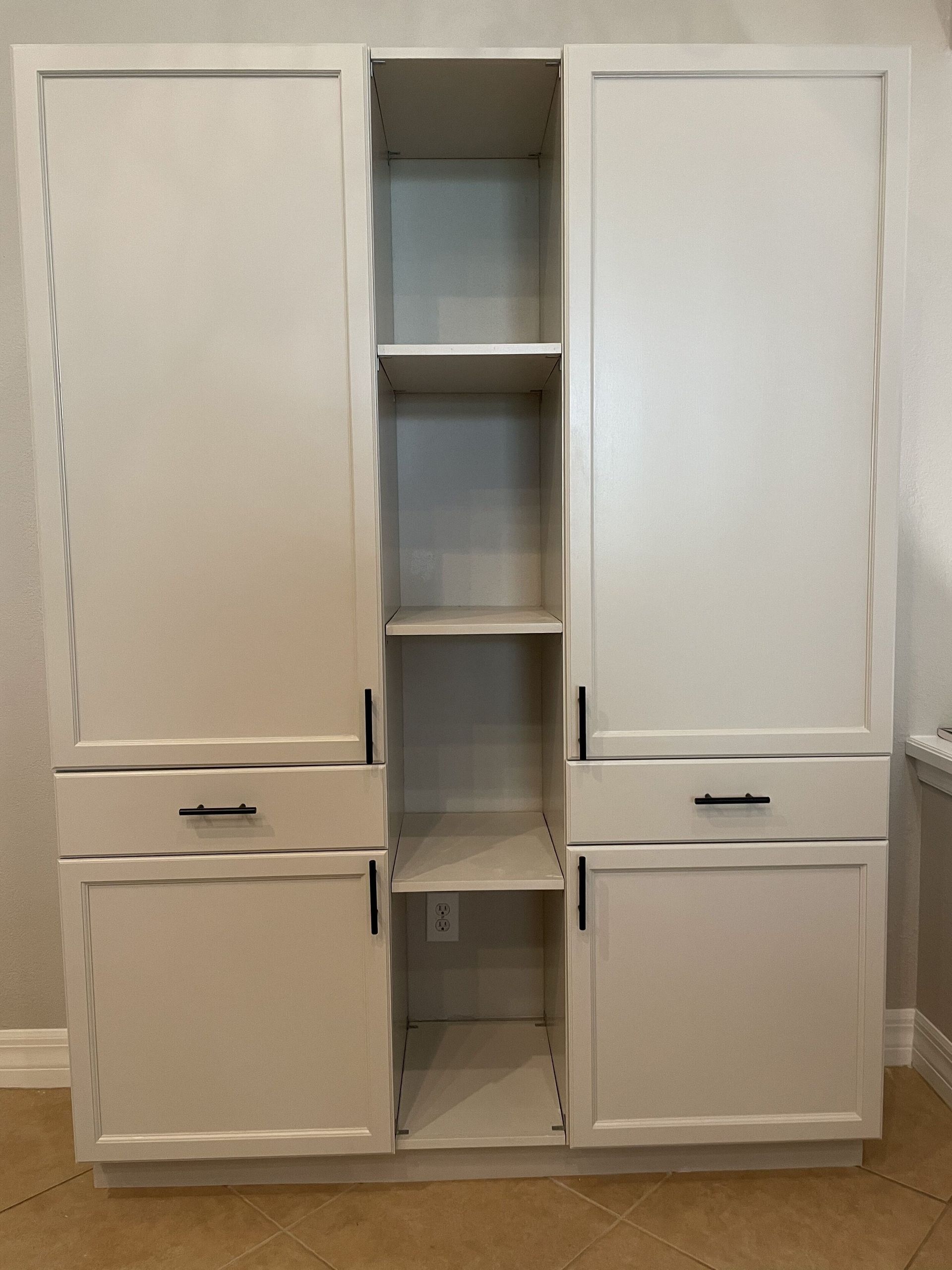 White kitchen cabinets with a central open shelf section and a wall outlet.