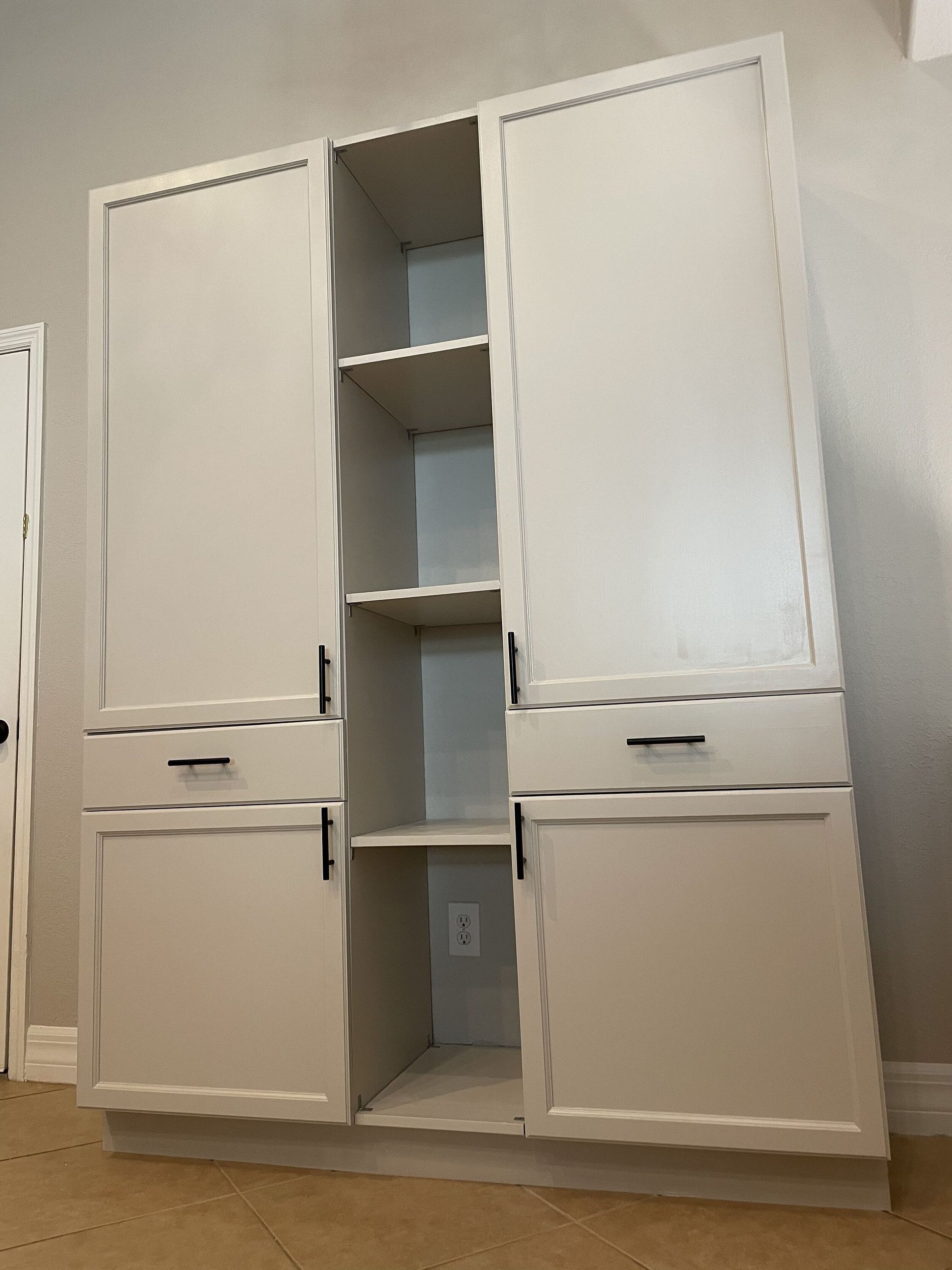White storage cabinet with two doors, shelves and drawers against a beige wall.