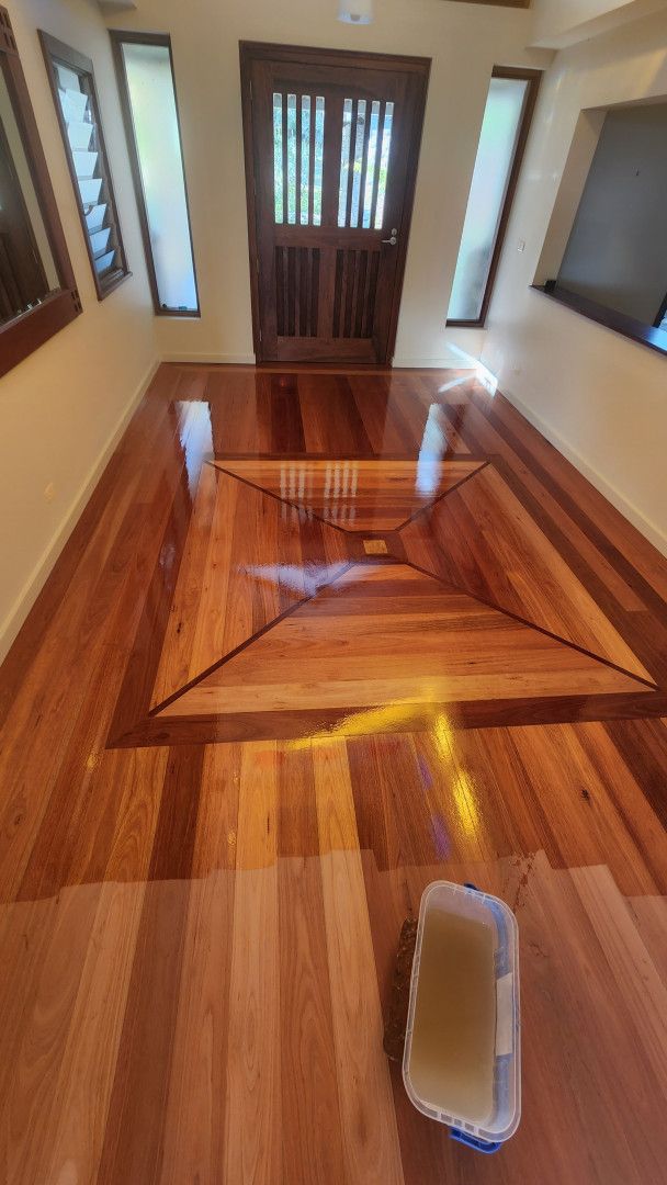 A Person is Using a Spatula to Spread White Paint on a Wooden Floor — Shane Callinan Floor Sanding In North Haven, NSW