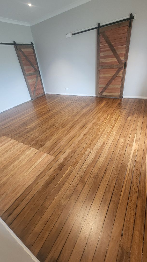 A Person is Painting a Wooden Deck With a Roller — Shane Callinan Floor Sanding In North Haven, NSW