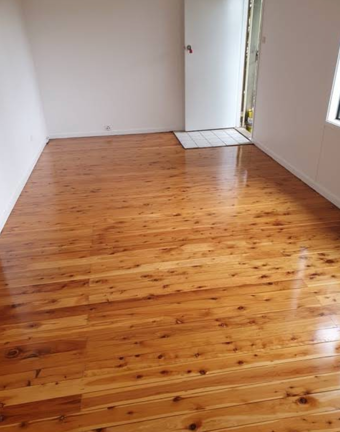 A Man is Applying Glue to a Wooden Floor — Shane Callinan Floor Sanding In North Haven, NSW