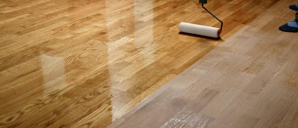 A Person is Painting a Wooden Floor With a Roller — Shane Callinan Floor Sanding In North Haven, NSW