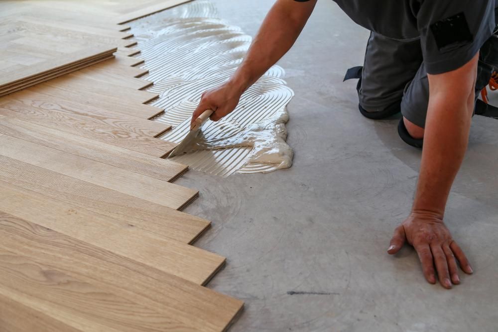 A Man is Applying Glue to a Wooden Floor — Shane Callinan Floor Sanding In Kempsey, NSW
