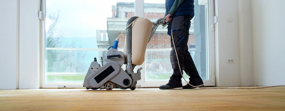 A Man is Sanding a Wooden Floor With a Machine — Shane Callinan Floor Sanding In Bonny Hills, NSW