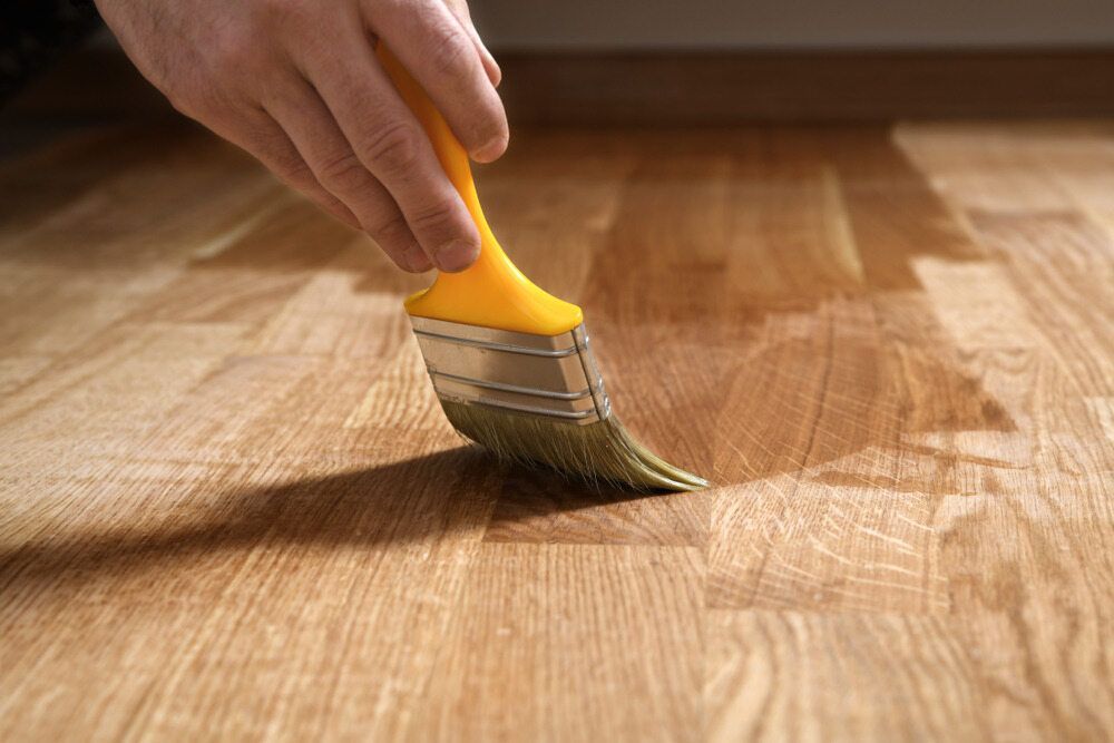 A Person is Painting a Wooden Floor With a Brush — Shane Callinan Floor Sanding In Wauchope, NSW