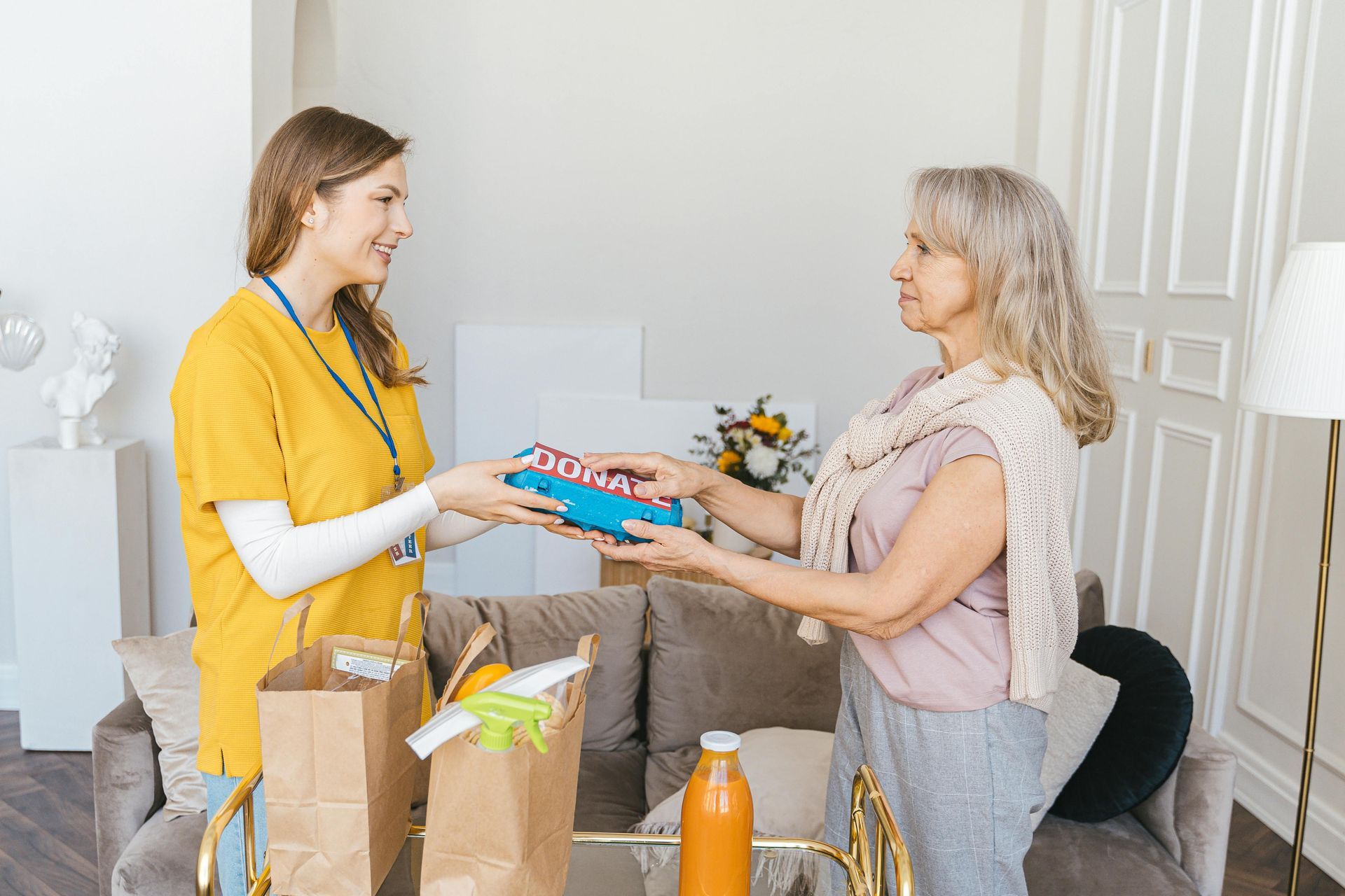 A woman is giving a gift to an elderly woman in a living room.