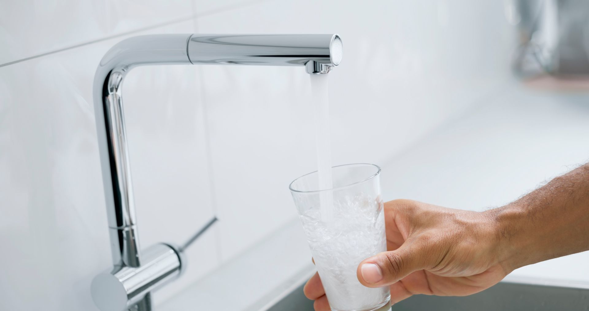 Man filling glass with clean water from residential water softening equipment system at home. Man filling glass with clean water from residential water softening equipment system at home.