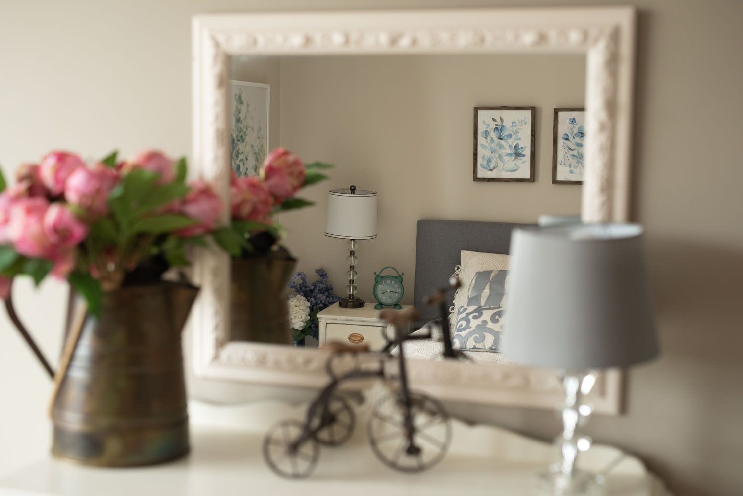 A vase of pink flowers sits on a table next to a mirror.