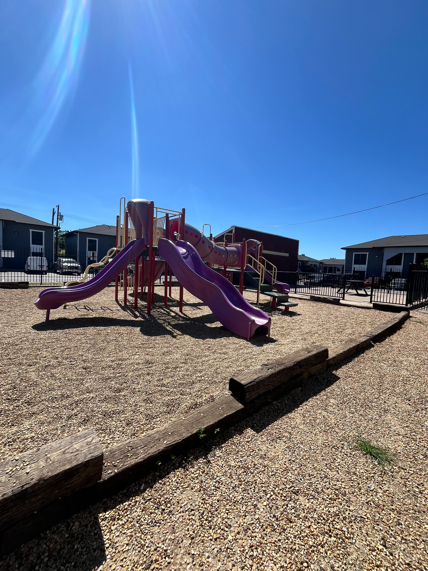 Playground with purple slides and wood retaining wall under a blue sky.