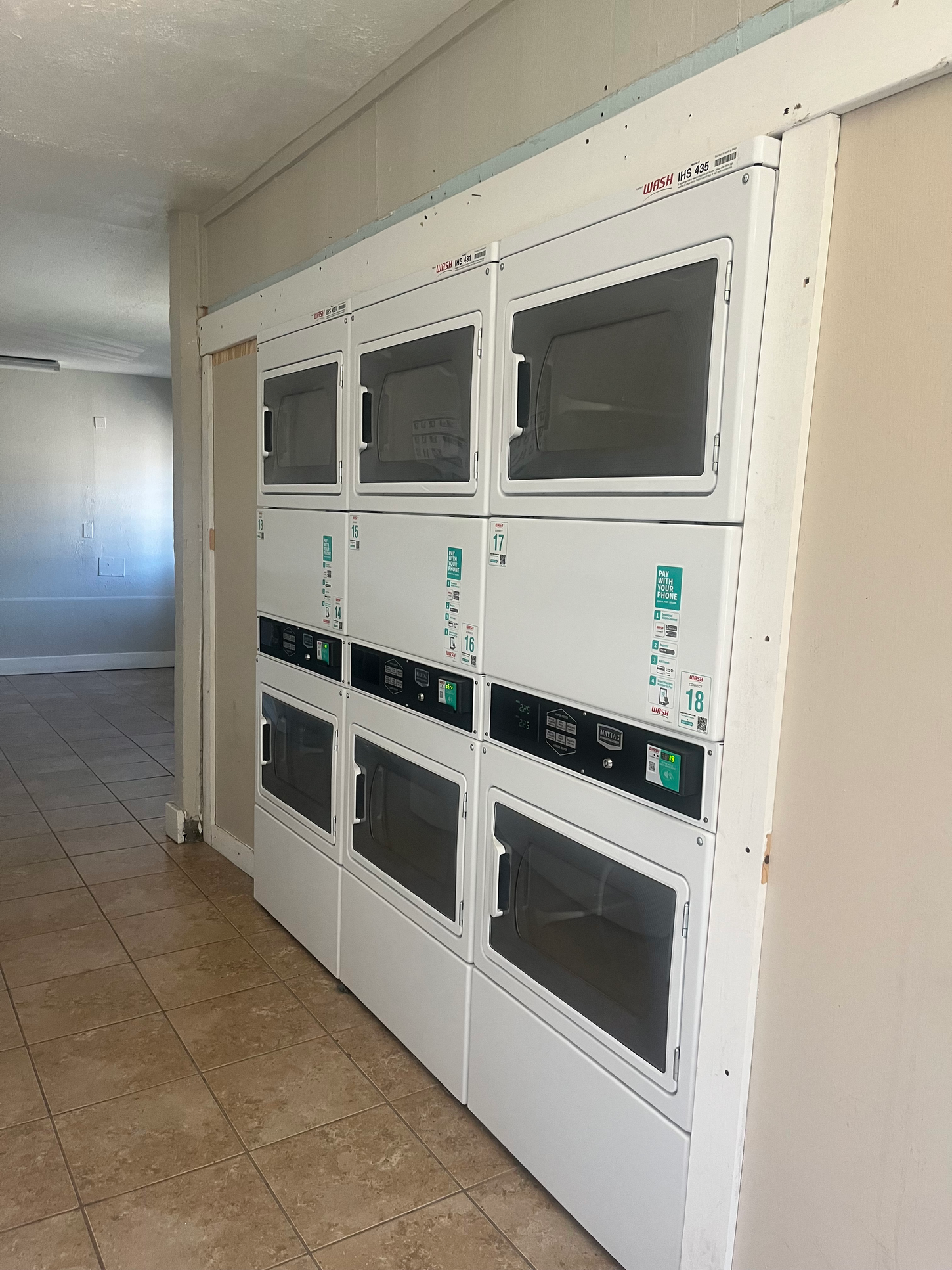 Nine white, coin-operated dryers in a laundry room. The dryers are stacked in three rows.