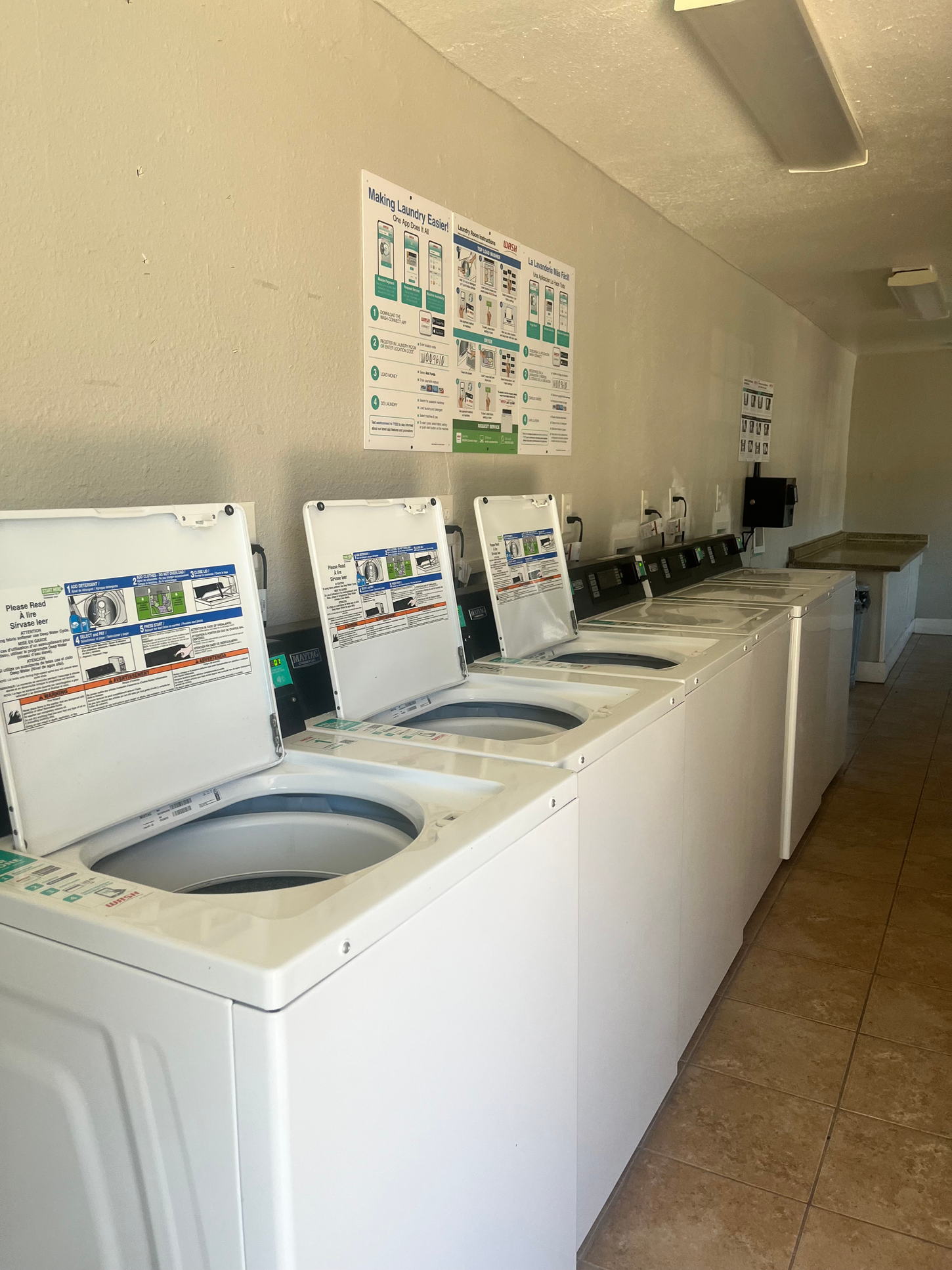 A laundromat with several white washing machines. Instructions hang on the wall.