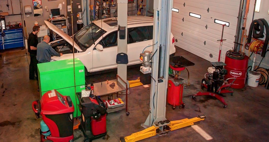 Car being serviced on a lift in a garage. Two people work on the engine; various tools and equipment surround the car. | Absolute Auto Repairs & Sales