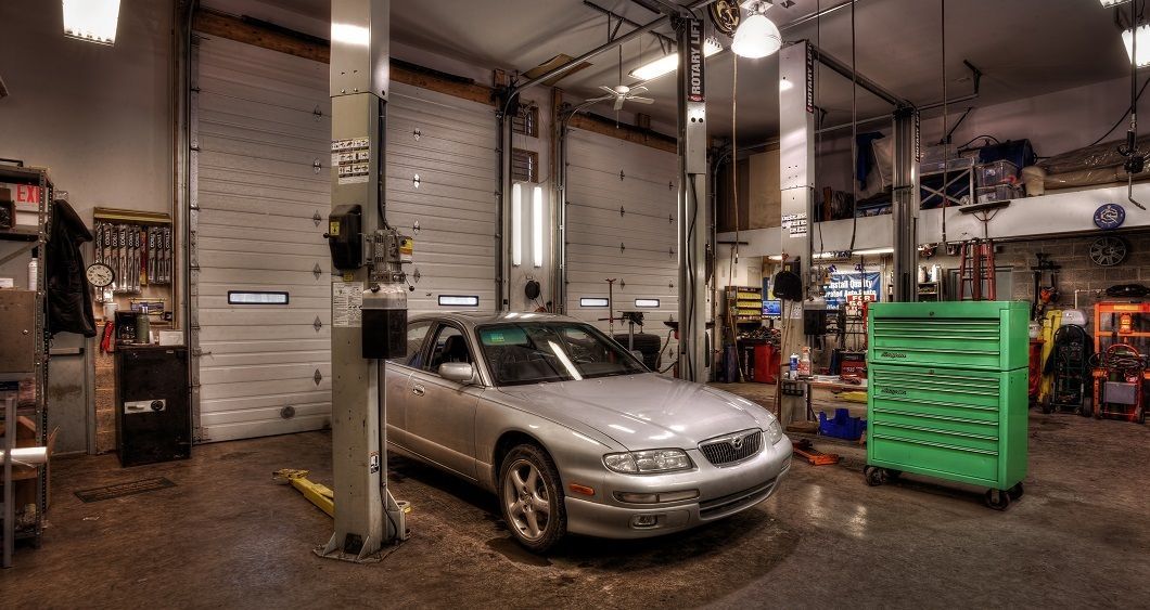 Silver car inside a well-lit auto repair shop with tools, lift, and green tool chest. | Absolute Auto Repairs & Sales