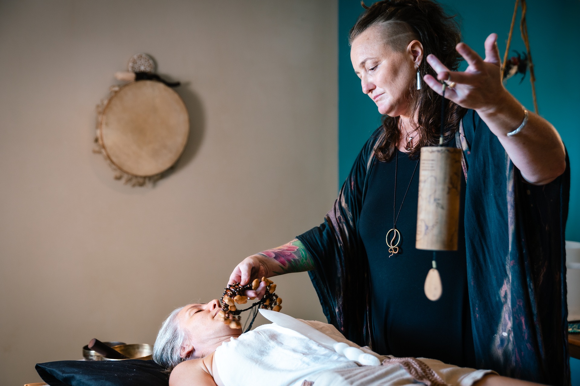 A woman is holding a bell over a woman laying on a bed.