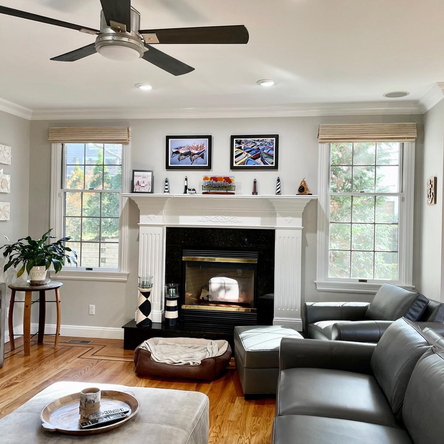 Living room with fireplace, gray sofa, wooden floors, windows, and ceiling fan.