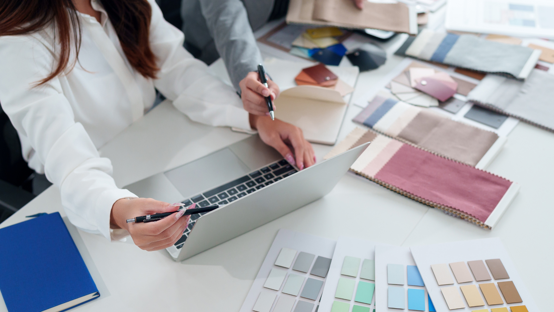Two people collaborating at a table with laptop, fabric swatches, and color palettes.