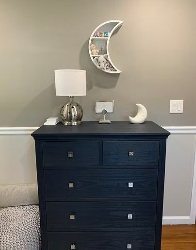 Navy dresser with lamp, moon shelf, and decor against a gray wall.