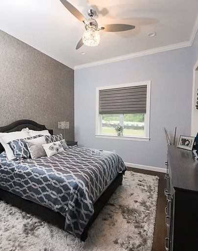Bedroom with a gray patterned bedspread, white trim, and a shaggy gray rug.